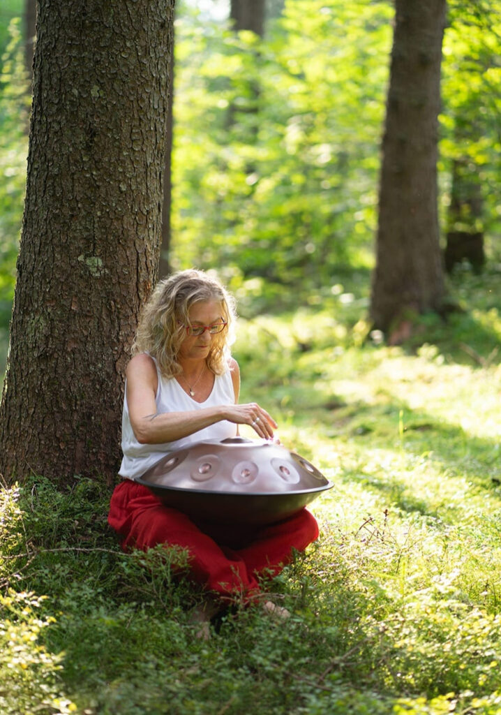 eike Wangler sitzt barfuß im Grünen und spielt meditativ auf einer Handpan